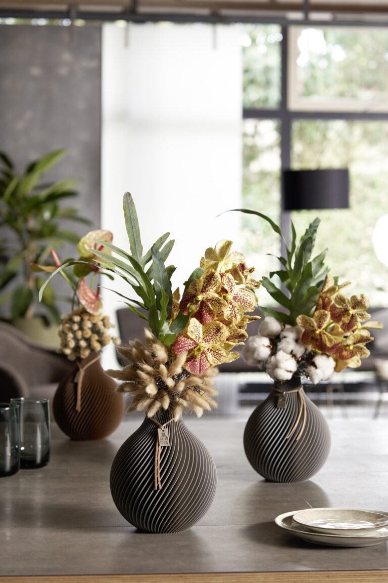 Moderni vasi di plastica organica riempiti di orchidee, anthurium e fiori secchi si trovano su un tavolo in un ambiente di vita moderno