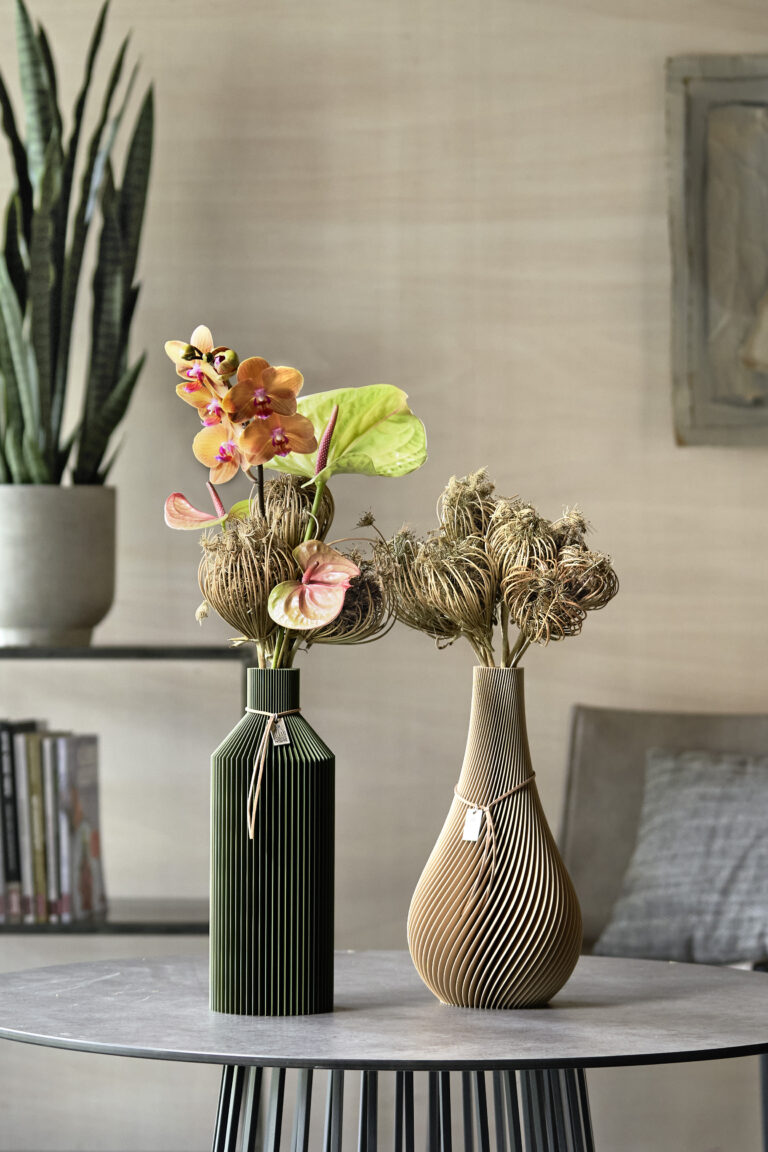 Moderni vasi di plastica organica riempiti con orchidea Phalaenopsis, fiore di fenicottero e carota selvatica si trovano su un tavolino in un ambiente moderno.